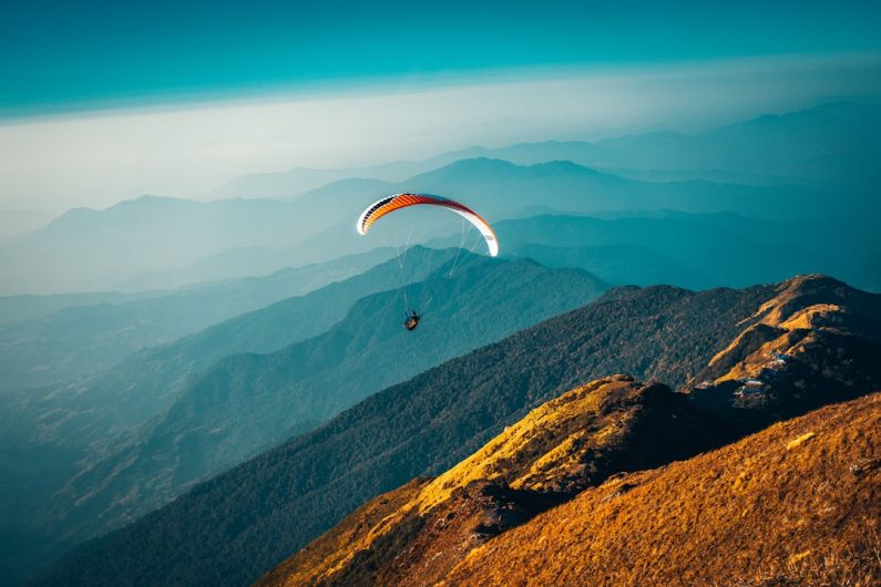 Adventure Travel - person in parachute over mountains during daytime
