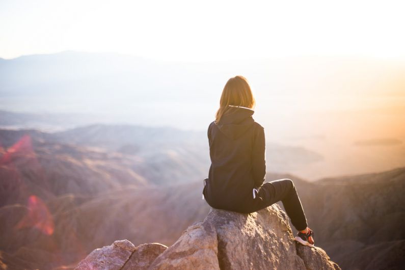 Future Travel - person sitting on top of gray rock overlooking mountain during daytime